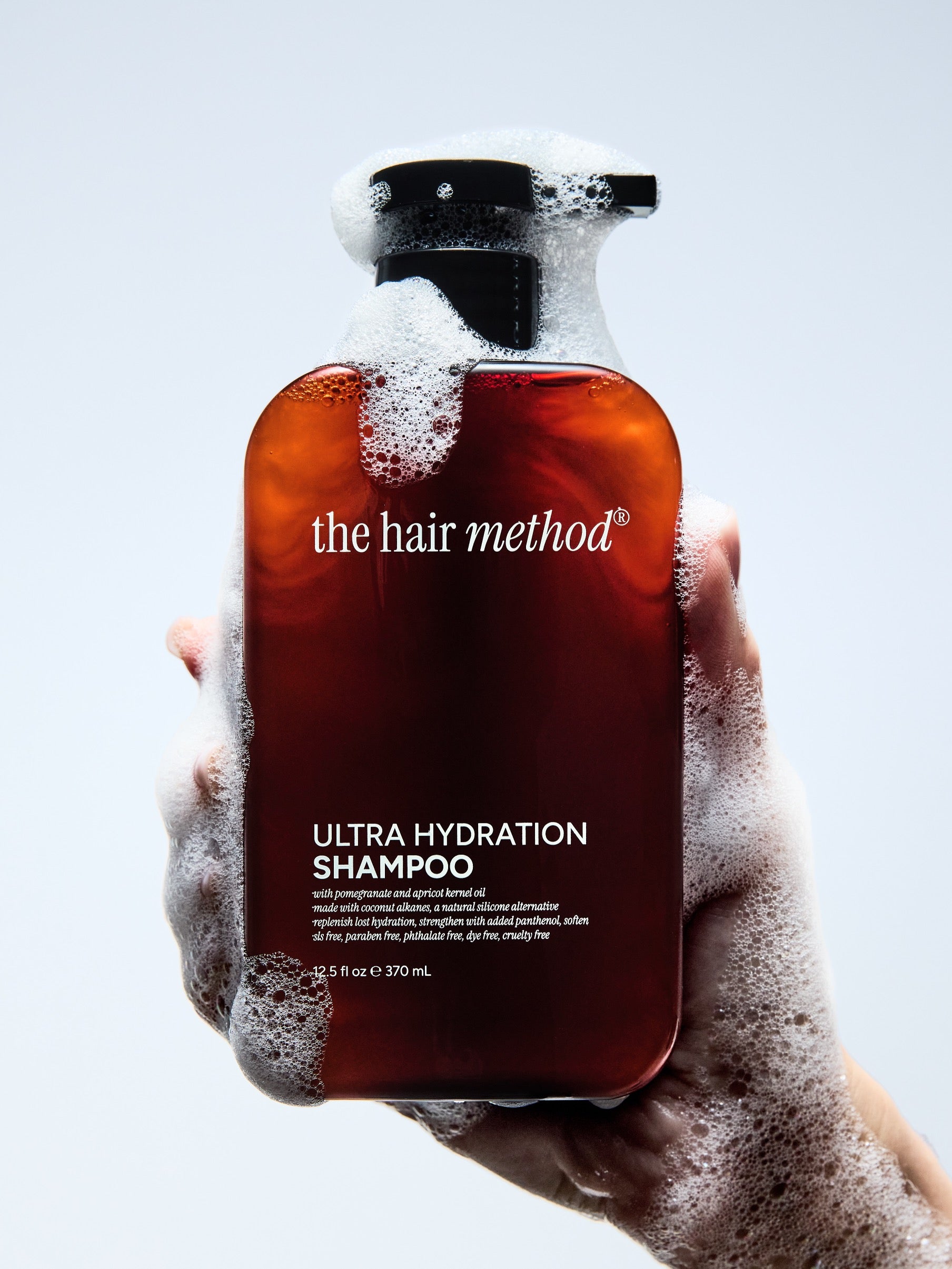 Hand holding a bottle of 'the hair method' Ultra Hydration Shampoo with a white background