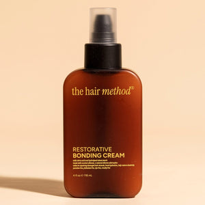 photograph of the front of a brown bottle with black pump and light orange text printed on it. the product is on a tan background with a large shadow behind it. it reads The Hair Method Restorative Bonding Cream.