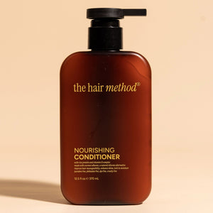 photograph of the front of a brown bottle with black pump and light orange text printed on it. the product is on a tan background with a large shadow behind it. it reads The Hair Method Nourishing Conditioner.