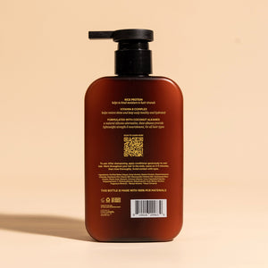 photograph of the back of a brown bottle with black pump and light green text printed on it. the product is on a tan background with a large shadow behind it