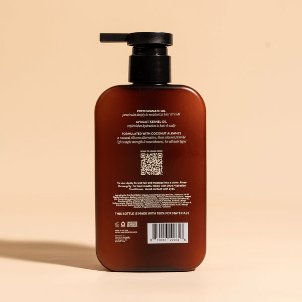 photograph of the back of a brown bottle with black pump and light green text printed on it. the product is on a tan background with a large shadow behind it