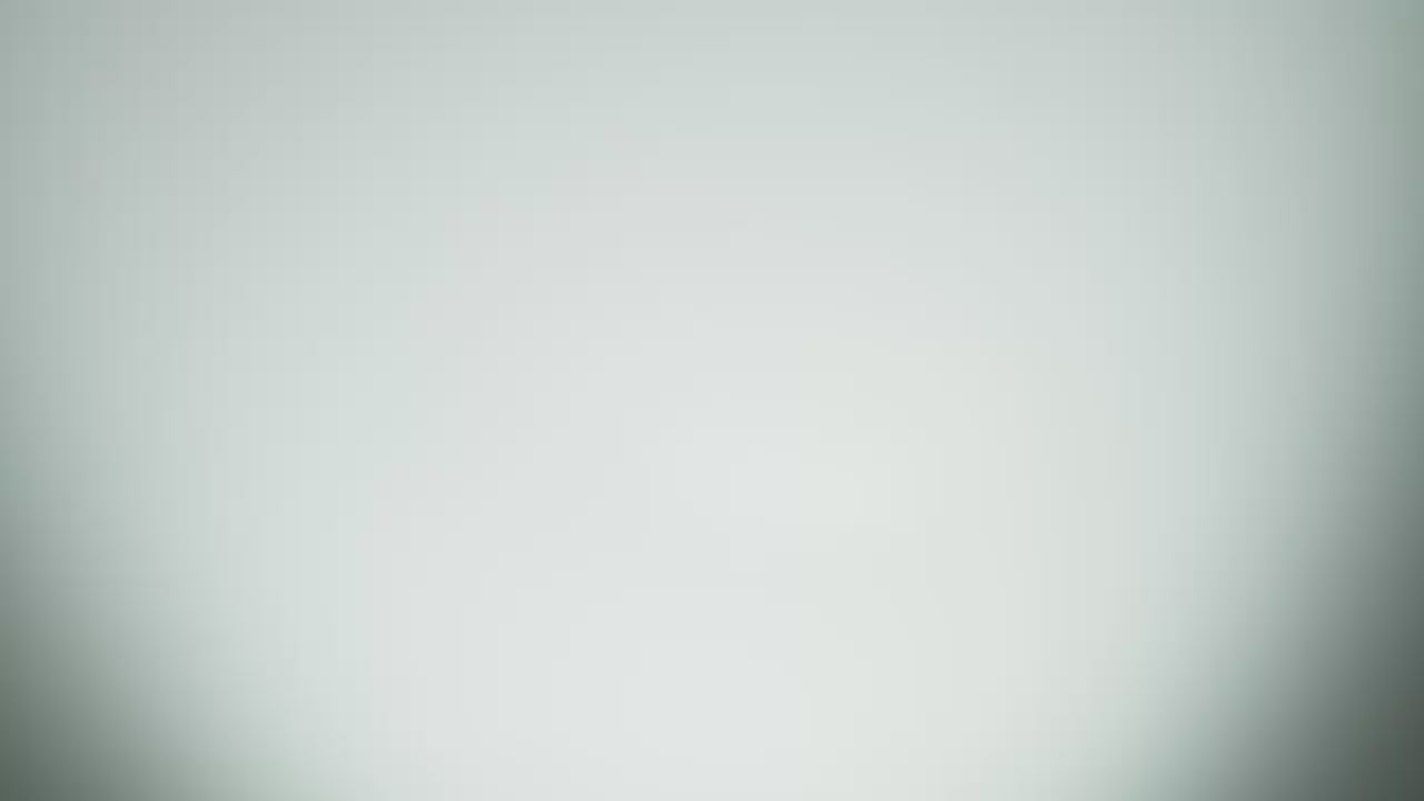 A slow motion video of two coconuts hitting each other mid air and breaking apart, causing coconut water to splash. There is no audio.