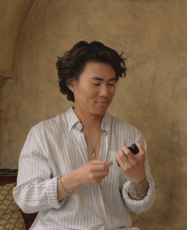 A short two second video of a young asian man spritzing a product towards the camera and laughing. there is no audio