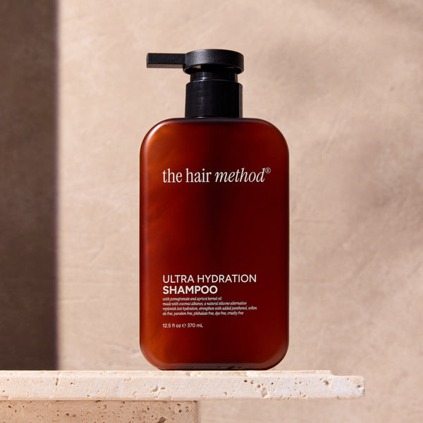 Amber shampoo bottle labeled 'the hair method' on a beige surface with a neutral background