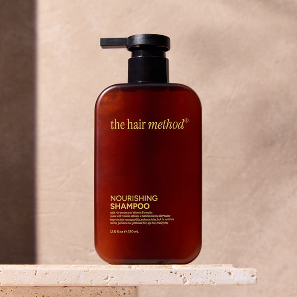 Brown shampoo bottle with pump labeled 'the hair method' on a beige surface.