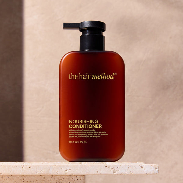The Hair Method nourishing conditioner bottle on a stone surface with a neutral background