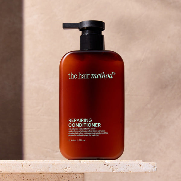 Brown bottle of 'the hair method' repairing conditioner on a beige surface with a neutral background