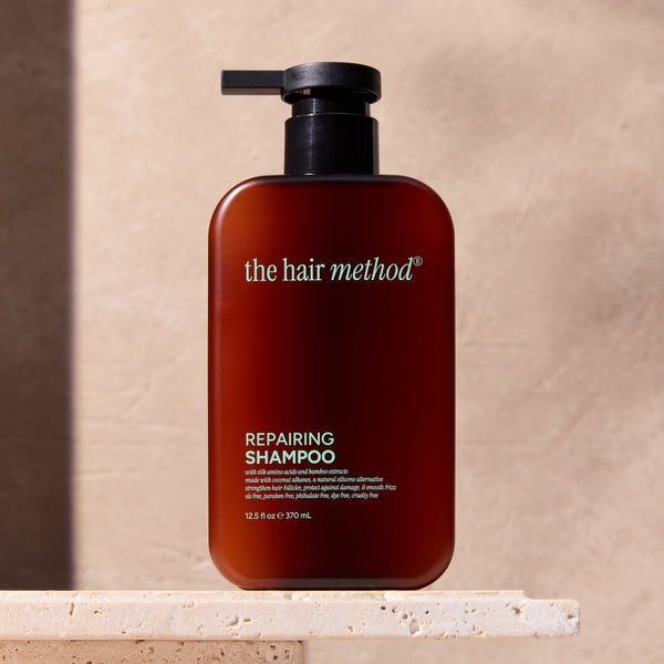 The Hair Method repairing shampoo bottle on a stone surface with a neutral background