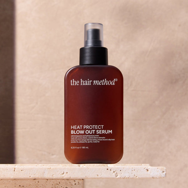 Bottle of 'the hair method' heat protect blowout serum on a beige surface with a neutral background