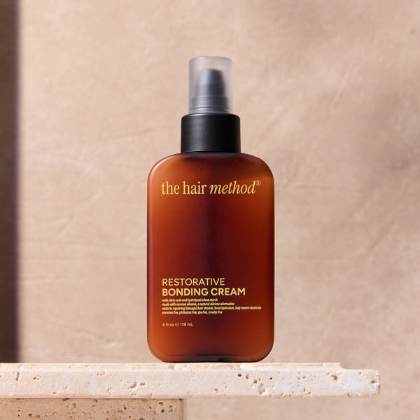 Bottle of 'the hair method' restorative bonding cream on a stone surface with a neutral background