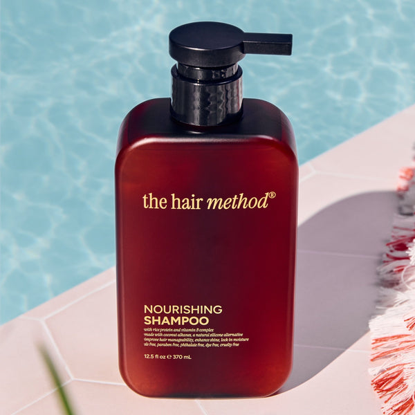 Amber shampoo bottle labeled 'the hair method' on a white surface with a pool in the background