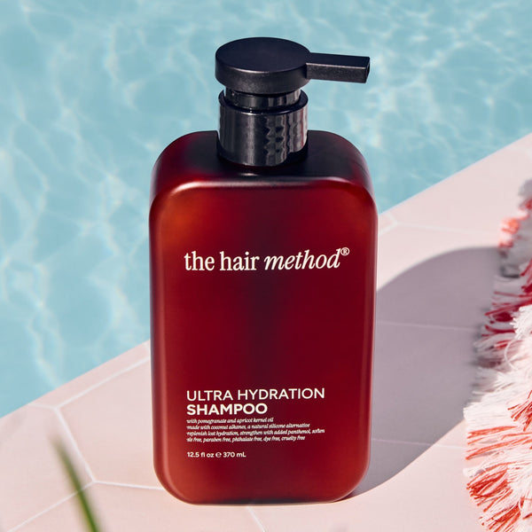 Amber shampoo bottle labeled 'the hair method' by a poolside with a towel and plant.