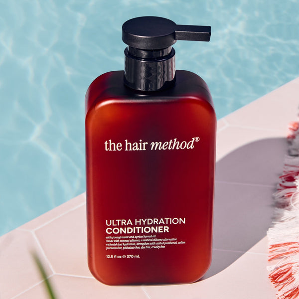 Amber bottle of 'the hair method' Ultra Hydration Conditioner on a ledge with water in the background
