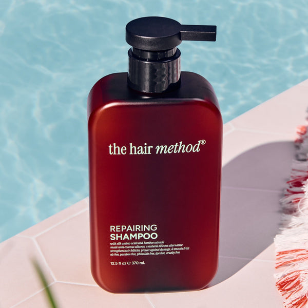 Amber shampoo bottle labeled 'the hair method' on a ledge with water in the background
