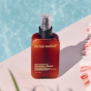 The hair method restorative bonding cream bottle on a poolside ledge with a towel.