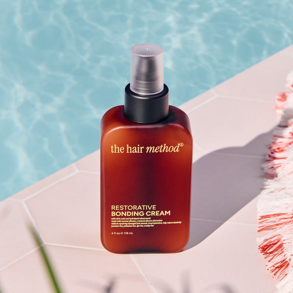 The hair method restorative bonding cream bottle on a poolside ledge with a towel.