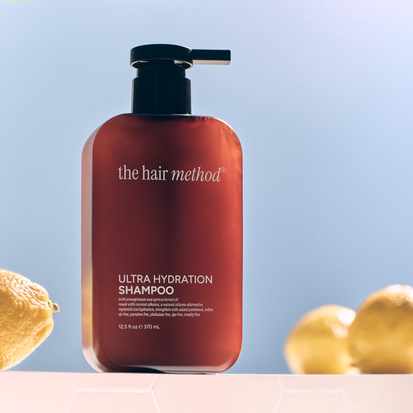Amber shampoo bottle with pump labeled 'the hair method' on a light blue background with lemons and leaves.