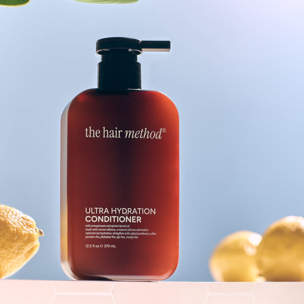 Amber bottle of 'the hair method' Ultra Hydration Conditioner with lemons and leaves on a light blue background