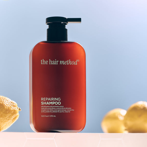 Amber shampoo bottle with pump labeled 'the hair method' on a light blue background with lemons and leaves.