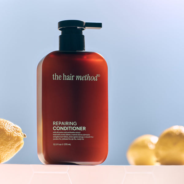 Amber bottle of 'the hair method' repairing conditioner with lemons and leaves on a light blue background