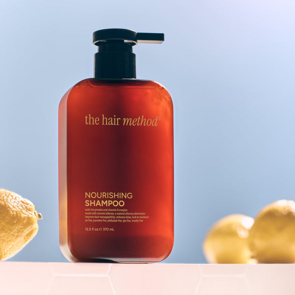 Amber shampoo bottle with pump labeled 'the hair method' on a light blue background with lemons and leaves.