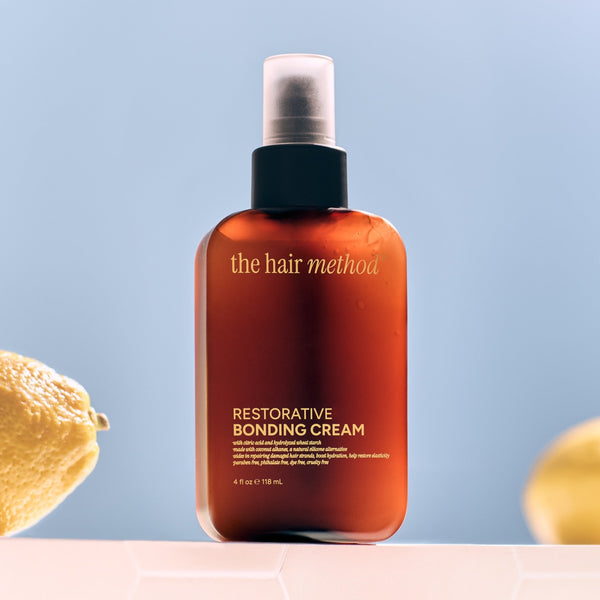 Bottle of 'the hair method' Restorative Bonding Cream with lemons and leaves on a light blue background